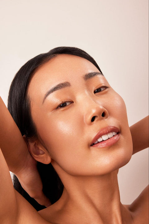 A woman with clear skin stretches to pull her hair back.