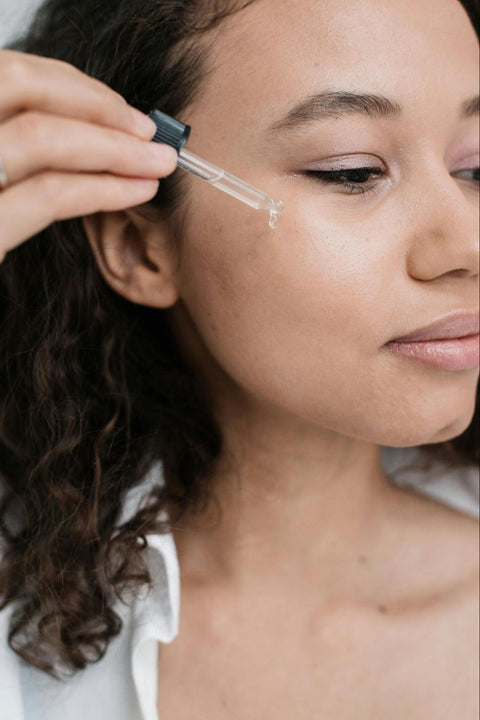 A woman uses a dropper to put serum on her face.