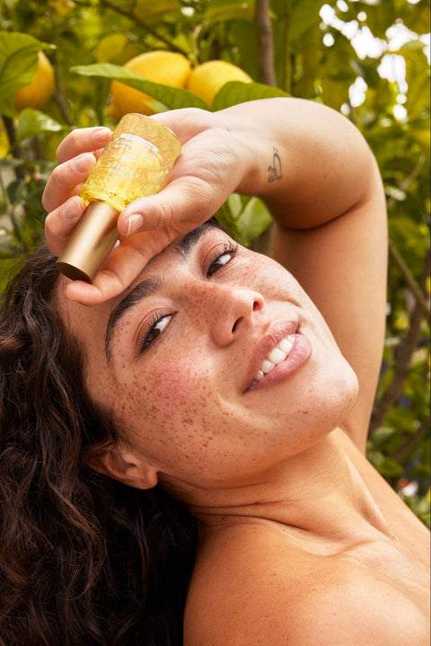 A woman with healthy skin holds a bottle of niacinamide-containing serum.